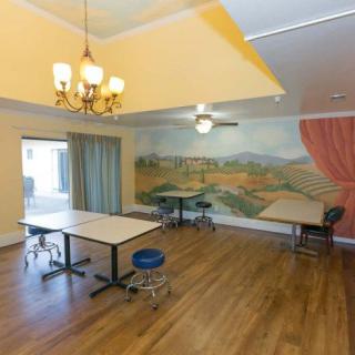 A spacious dining area with tables, chairs, a mural on the wall, and warm lighting from a chandelier and ceiling fan.