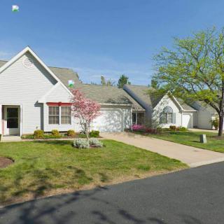 A suburban home with a driveway, garden, and blooming trees on a sunny spring day.