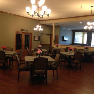 A cozy dining room with neatly arranged tables and chairs, illuminated by elegant chandeliers.