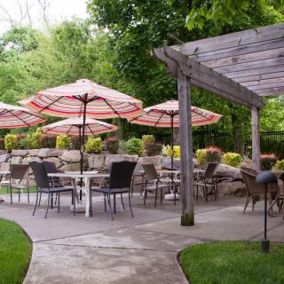 A serene outdoor patio area with tables, chairs, and red-striped umbrellas surrounded by lush greenery.