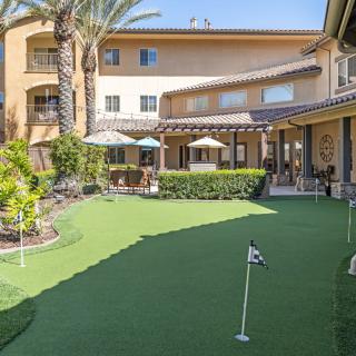 A sunny courtyard with a small putting green and patio umbrellas surrounded by a residential building.