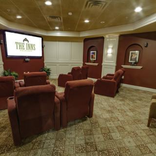 A cozy theater room with red chairs facing a large screen.