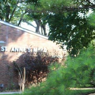 A brick building partially obscured by greenery, featuring a sign that reads 'St. Anne's'.