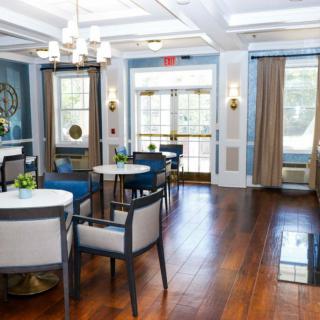 A modern dining area with elegant furnishings and wooden flooring, featuring bright natural light from large windows.