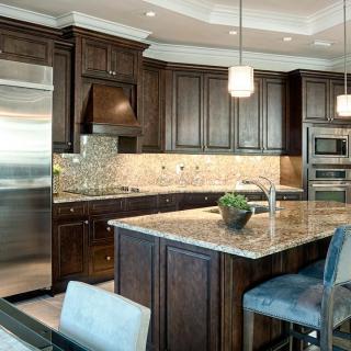 A modern kitchen featuring dark wood cabinets, a granite countertop island with seating, and pendant lighting.