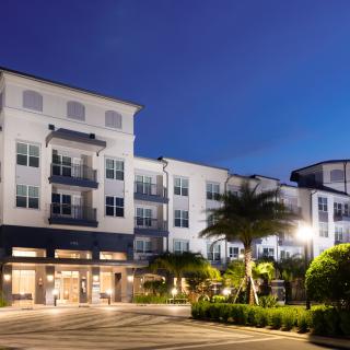 A modern residential building illuminated at night with palm trees in the foreground.