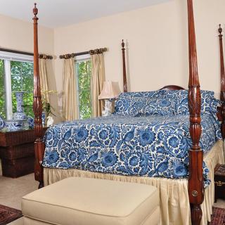 A cozy bedroom with a four-poster bed featuring blue patterned bedding, surrounded by elegant curtains and classic furniture.