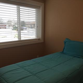 A minimalist bedroom with a single bed featuring turquoise bedding and a window allowing natural light to enter.