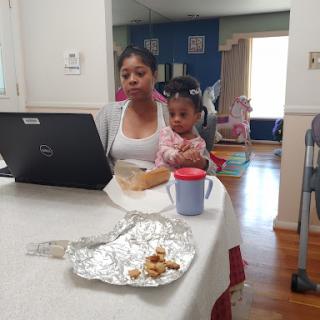 A mother works on her laptop while holding her child at home.