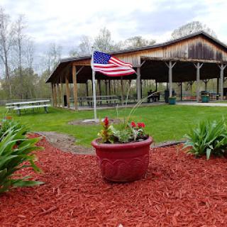 A peaceful park area featuring a U.S. flag, vibrant flowers, and a rustic pavilion.