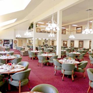 A spacious dining area with elegant chandeliers, neatly arranged tables and chairs, and a vibrant red carpet.