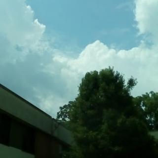 A view of a partly cloudy sky with a tree and building in the foreground.