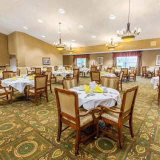 A spacious dining room with elegant furnishings and well-set tables, featuring chandeliers and a carpeted floor.