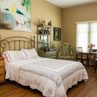 A cozy bedroom with a neatly made bed, decorative artwork, and a functional workspace.