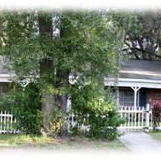 A cozy house surrounded by lush greenery and a white picket fence.