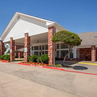 The entrance of a brick hotel with neatly trimmed bushes and clear skies.