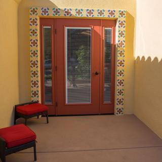 A patio features a decorative door with a colorful tile border and two red-cushioned chairs.