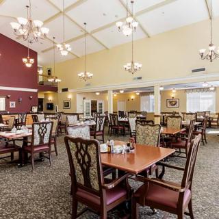 A spacious dining area with neatly arranged tables and chairs, illuminated by elegant chandeliers under a high ceiling.