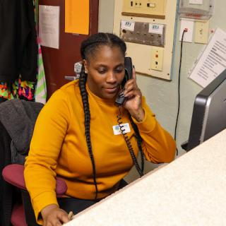A woman in an orange sweater engaged in a phone conversation at her desk.