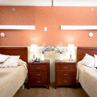 A cozy bedroom with two beds and a shared nightstand between them, adorned with lamps and wall lights.