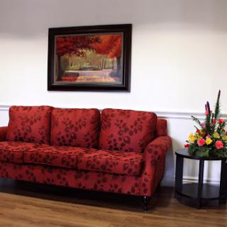 A beautifully decorated living room featuring a red floral sofa, vibrant artwork on the wall, and a small table with colorful flowers.