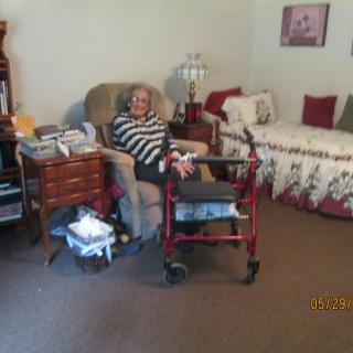 An elderly person sitting comfortably in a living room with a walker nearby.