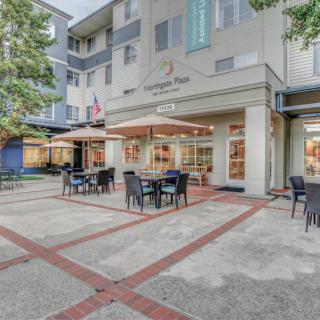 An outdoor cafe with tables and chairs under umbrellas, set in front of a modern building.