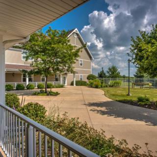 A charming house with a driveway, surrounded by trees and a well-maintained lawn under a partly cloudy sky.