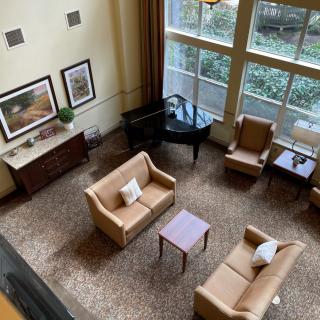 A cozy lobby area featuring sofas, armchairs, a coffee table, and a grand piano by large windows.
