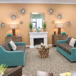 A cozy living room with teal sofas, a central coffee table, and a decorative fireplace.