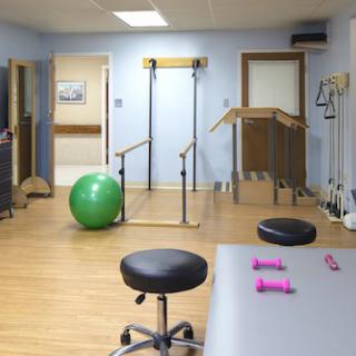 A physical therapy room equipped with parallel bars, a stability ball, and small dumbbells for rehabilitation exercises.