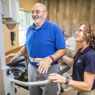 A trainer assists an elderly man during a rehabilitation exercise session.