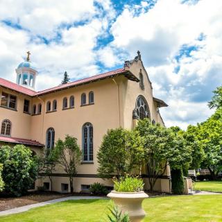 A historic church building with a lush garden and a cloudy sky.