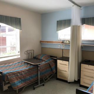 A view of a hospital patient room featuring two beds and essential furniture.