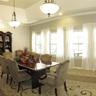 An elegant dining room with a long table, upholstered chairs, and large windows adorned with sheer curtains.