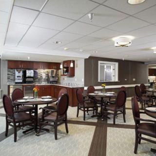 A modern dining area with round tables and chairs, featuring a visible kitchen area in the background.