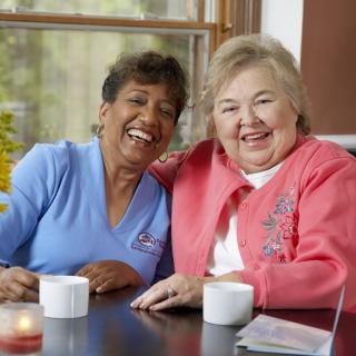 Two senior women enjoying coffee and laughing together indoors.