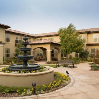 A tranquil courtyard featuring a central fountain surrounded by well-maintained landscaping and a two-story building.