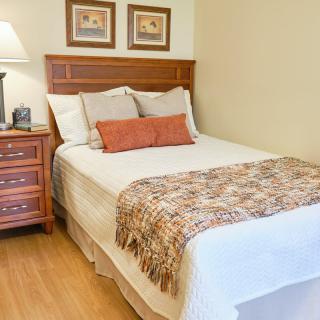 A cozy and well-decorated bedroom featuring a neatly made bed with a wooden headboard, accompanied by a nightstand and lamp.