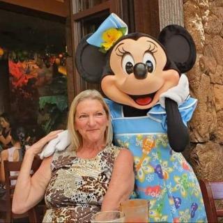 A woman poses with Minnie Mouse in a colorful outfit outdoors.