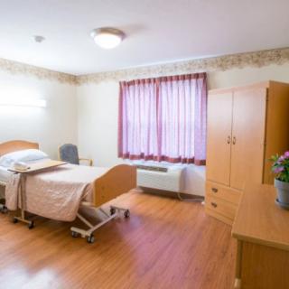 A clean and well-organized hospital room with a bed and wooden furniture.