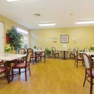 A spacious dining room with several empty tables and chairs, decorated with plants and artwork.