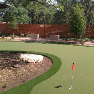 A backyard putting green with artificial turf and landscaping.