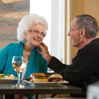 An elderly couple sharing a tender moment while dining together in a restaurant.