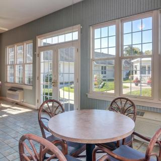 A bright sunroom with a circular table and chairs, featuring large windows letting in natural light.