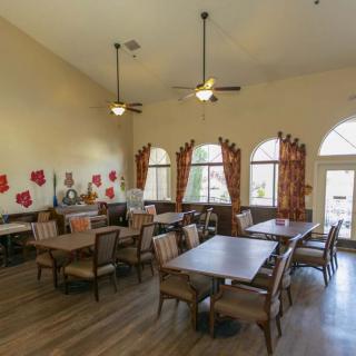 A spacious dining area with multiple tables and chairs, featuring large windows, ceiling fans, and decorative elements on the walls.