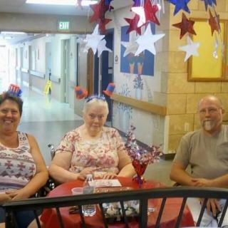 Three people sitting at a decorated table with patriotic-themed decorations in a hallway.