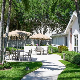 A serene garden patio with tables, chairs, and umbrellas surrounded by lush greenery.