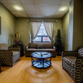 A cozy living room with a sofa, two armchairs, and a coffee table, accented by curtains and indoor plants.