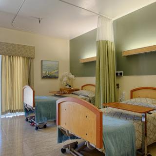 A spacious and well-lit hospital patient room featuring two beds, curtains for privacy, and a calming color palette.